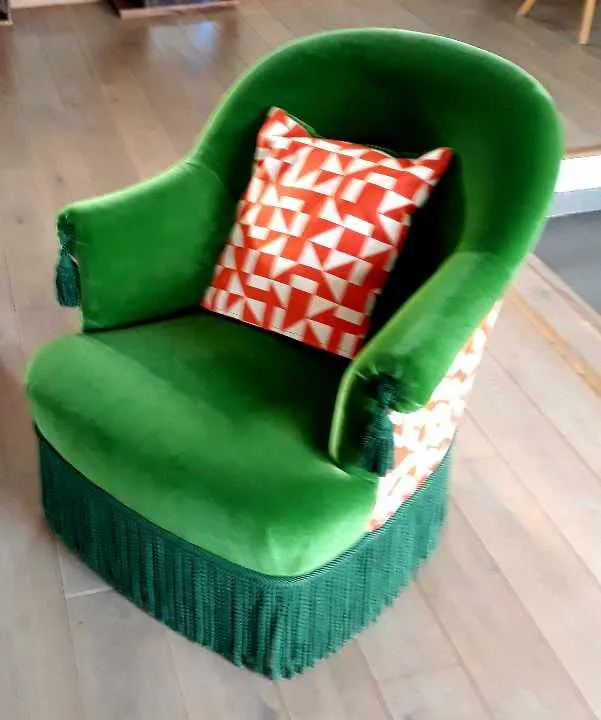 Fauteuil crapaud garni de velours vert, agrémenté d'un coussin à motif géométrique orange